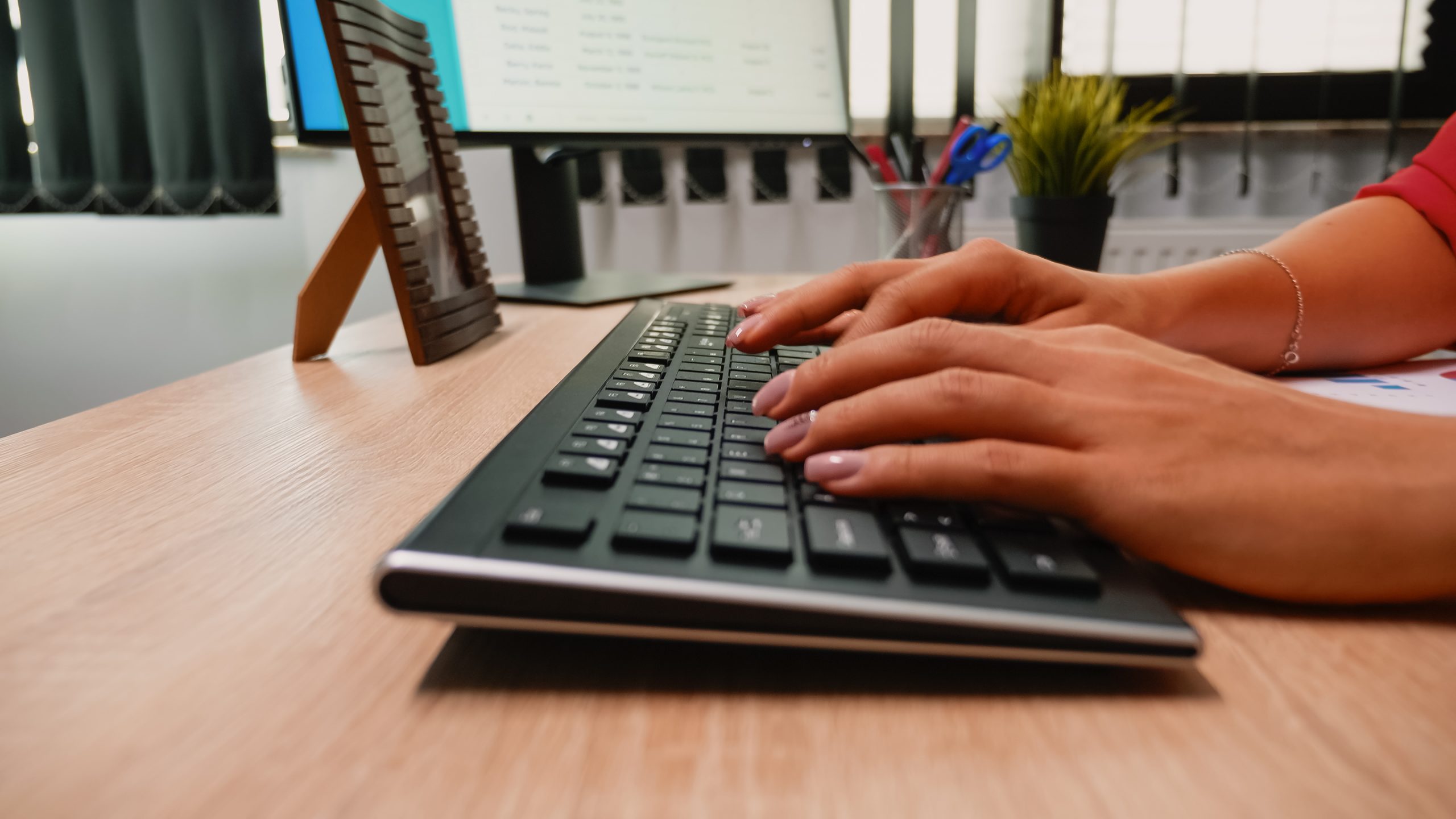 Close-up of moving shot with person typing on the computer keyboard. Freelancer working, writing emails, using internet sitting in front of computer in professional company workspace